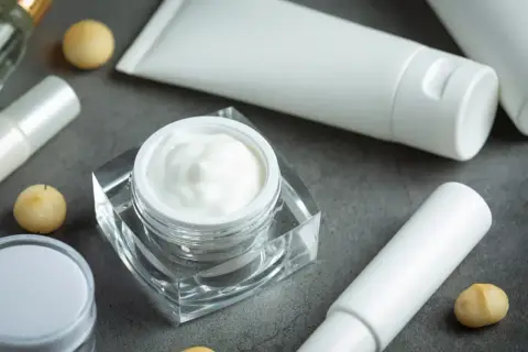 Crema blanca en un frasco de cristal, tubos y bolitas doradas. Descubre qué es el pantenol y sus beneficios para tu piel.